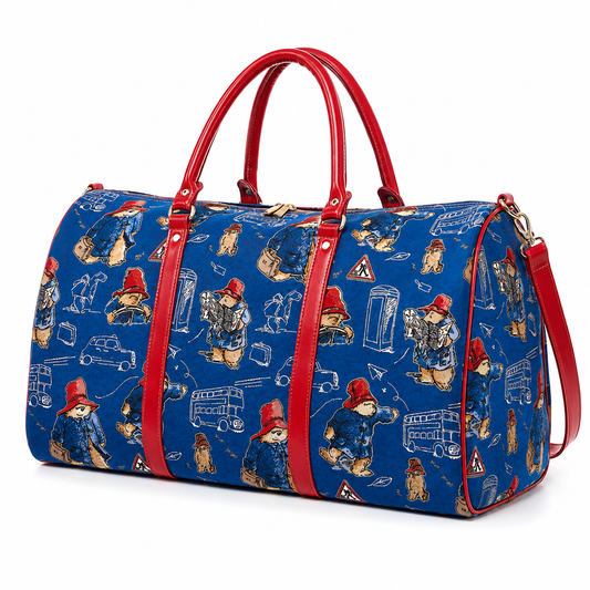 A blue duffel bag with a red leather handle and strap, covered in a repeating print of Paddington Bear illustrations, shown on a white background.