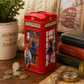 Red telephone box-shaped money box with children illustration on a wooden surface with coins and books.