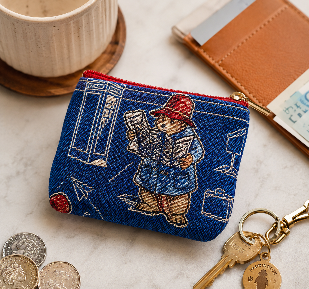 Blue coin purse with Paddington Bear design on a marble surface with coins and keys.