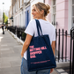 Woman carrying a tote bag with 'The Notting Hill Shopper Bag' text on a street.