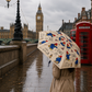 Person holding a Paddington Bear print umbrella on a rainy Westminster street, with Big Ben and a red telephone box in the background.