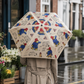 Outside the flower shop:
Person holding an open cream Paddington Bear print umbrella on a wet street beside a flower shop.